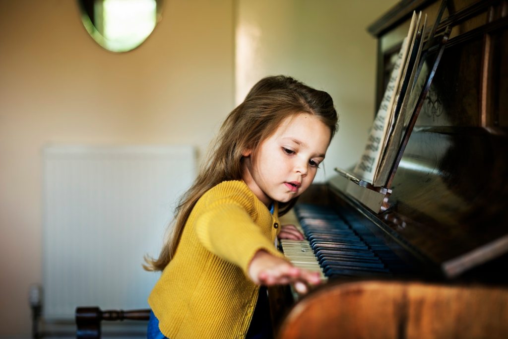young girl sitting beside a piano playing with the keys